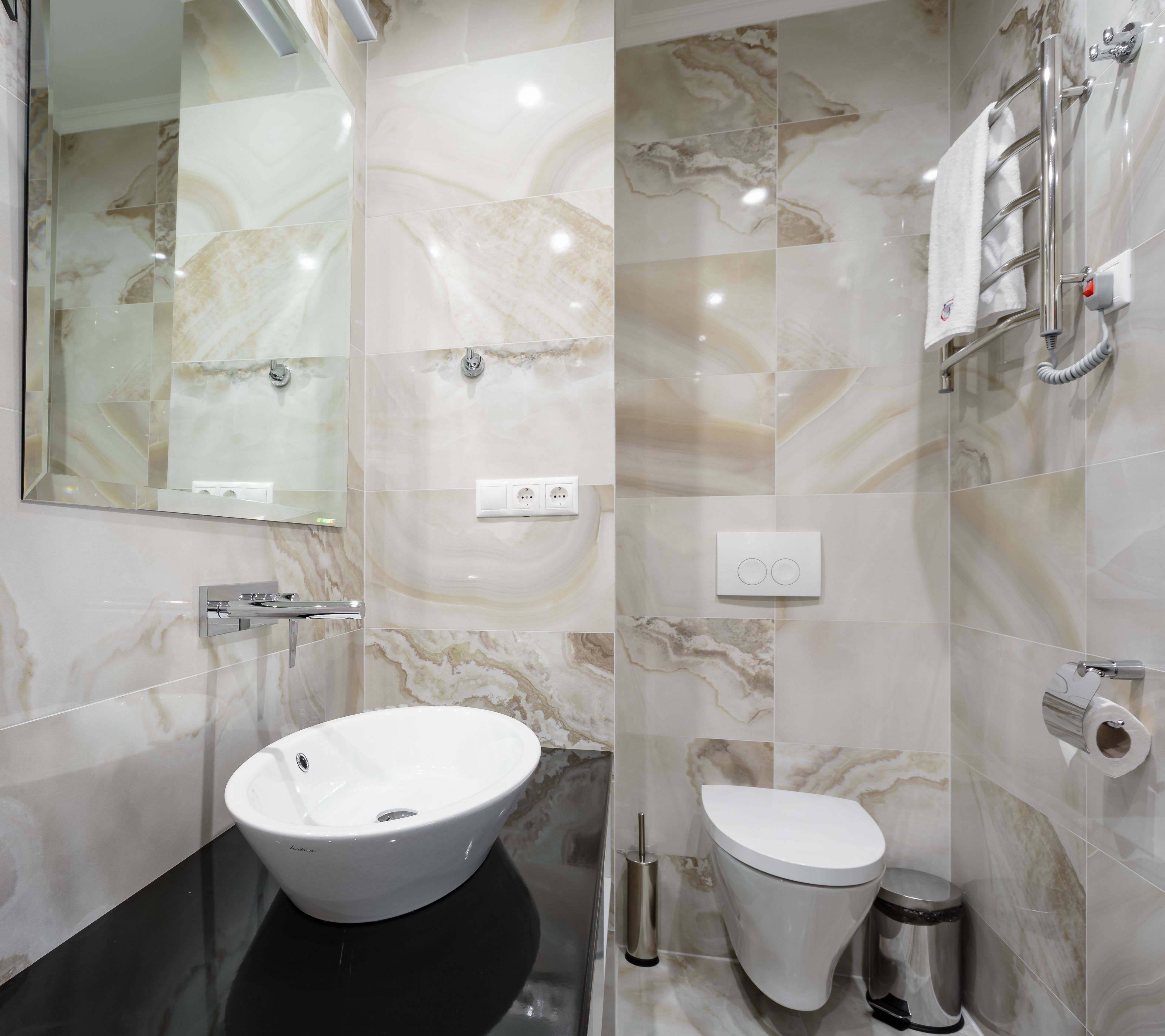 A modern bathroom with a large mirror, a white sink, a toilet, and a shower area.