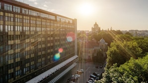 A modern hotel with a large glass facade, a central courtyard, and a view of a historic church in the background. - Premier Hotel Dnister (Lviv)