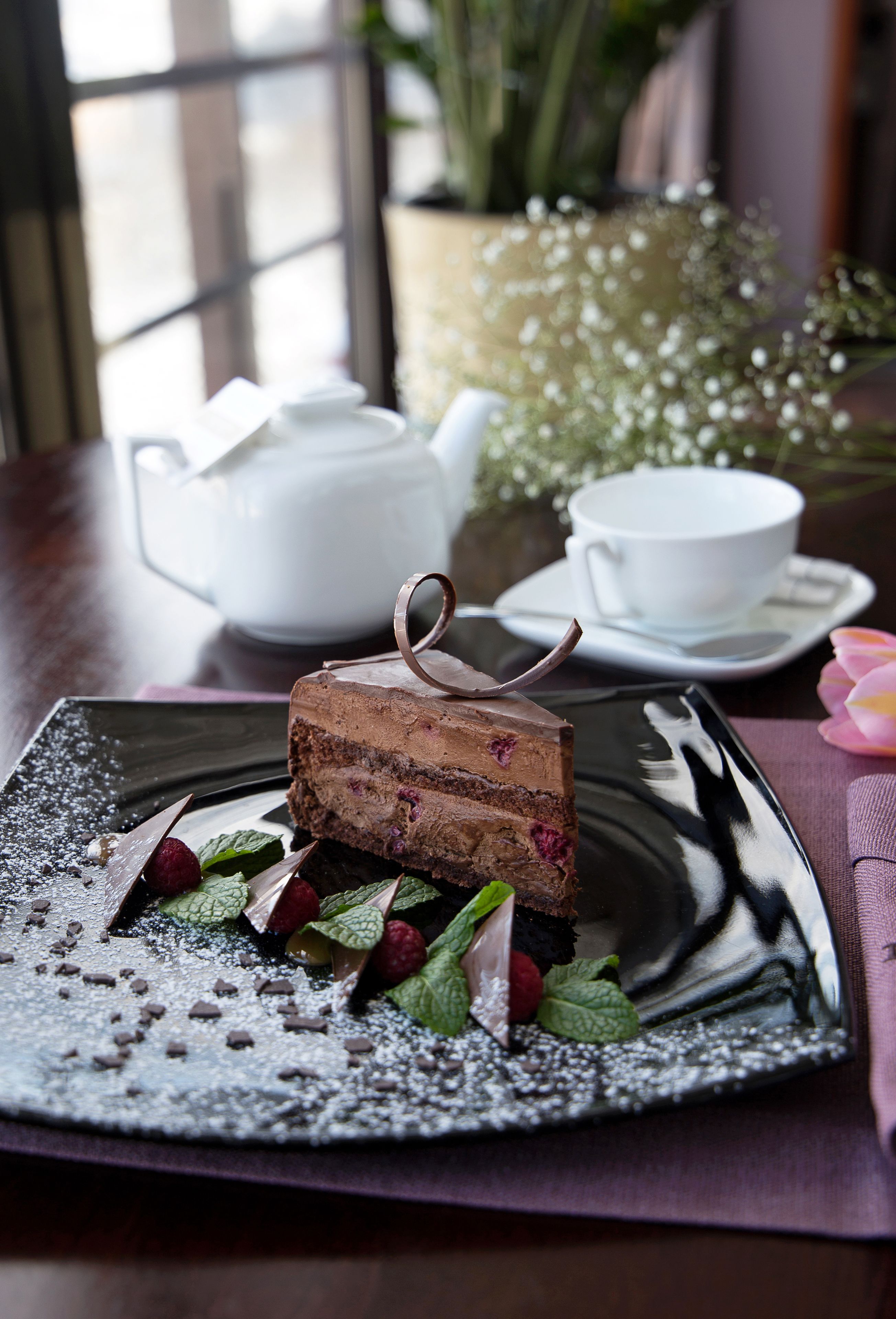A dessert on a plate with powdered sugar, mint leaves, and chocolate shavings.