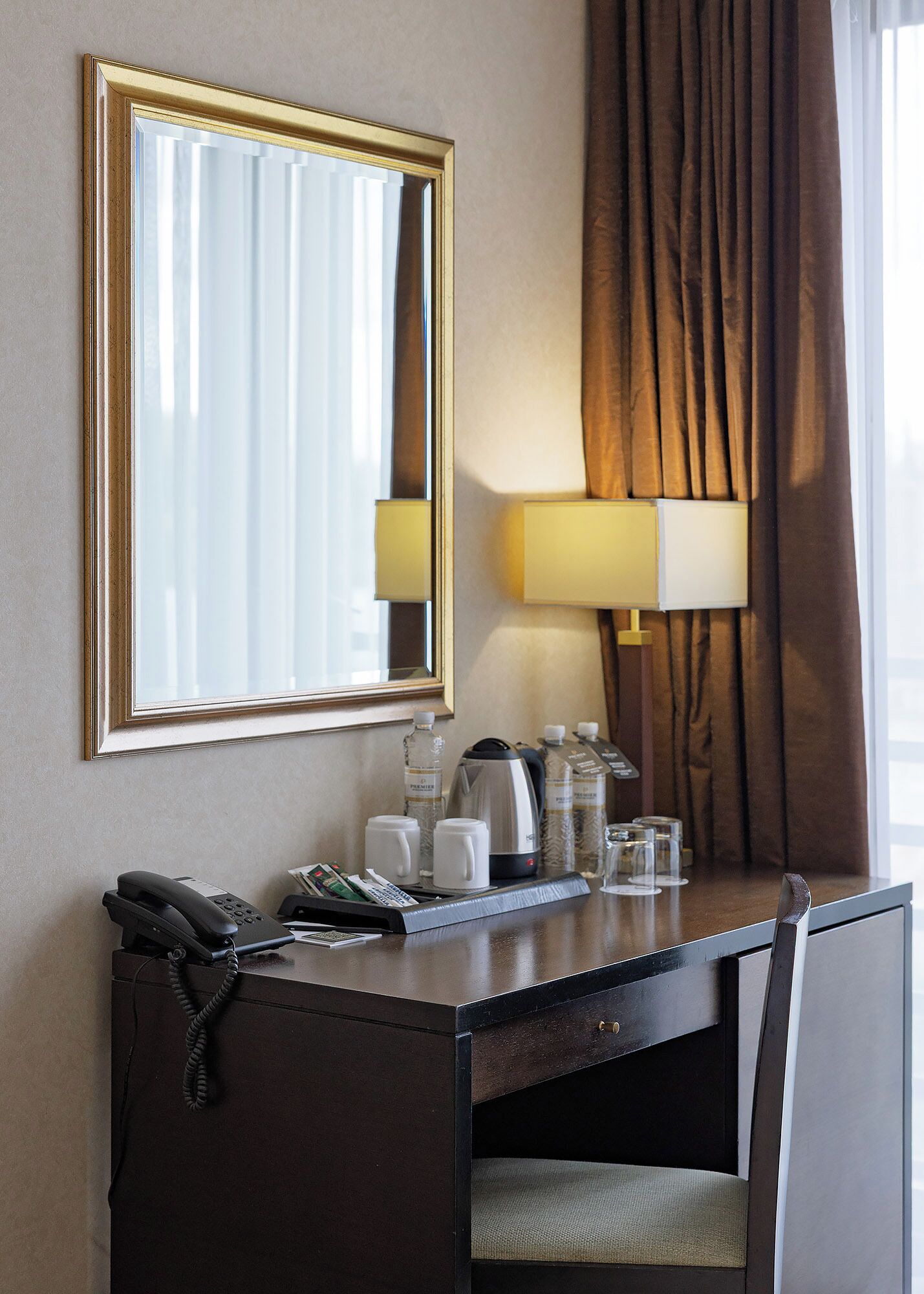 Ein Hotelzimmer mit Schreibtisch, Telefon, Lampe und einem Fenster mit Vorhängen.