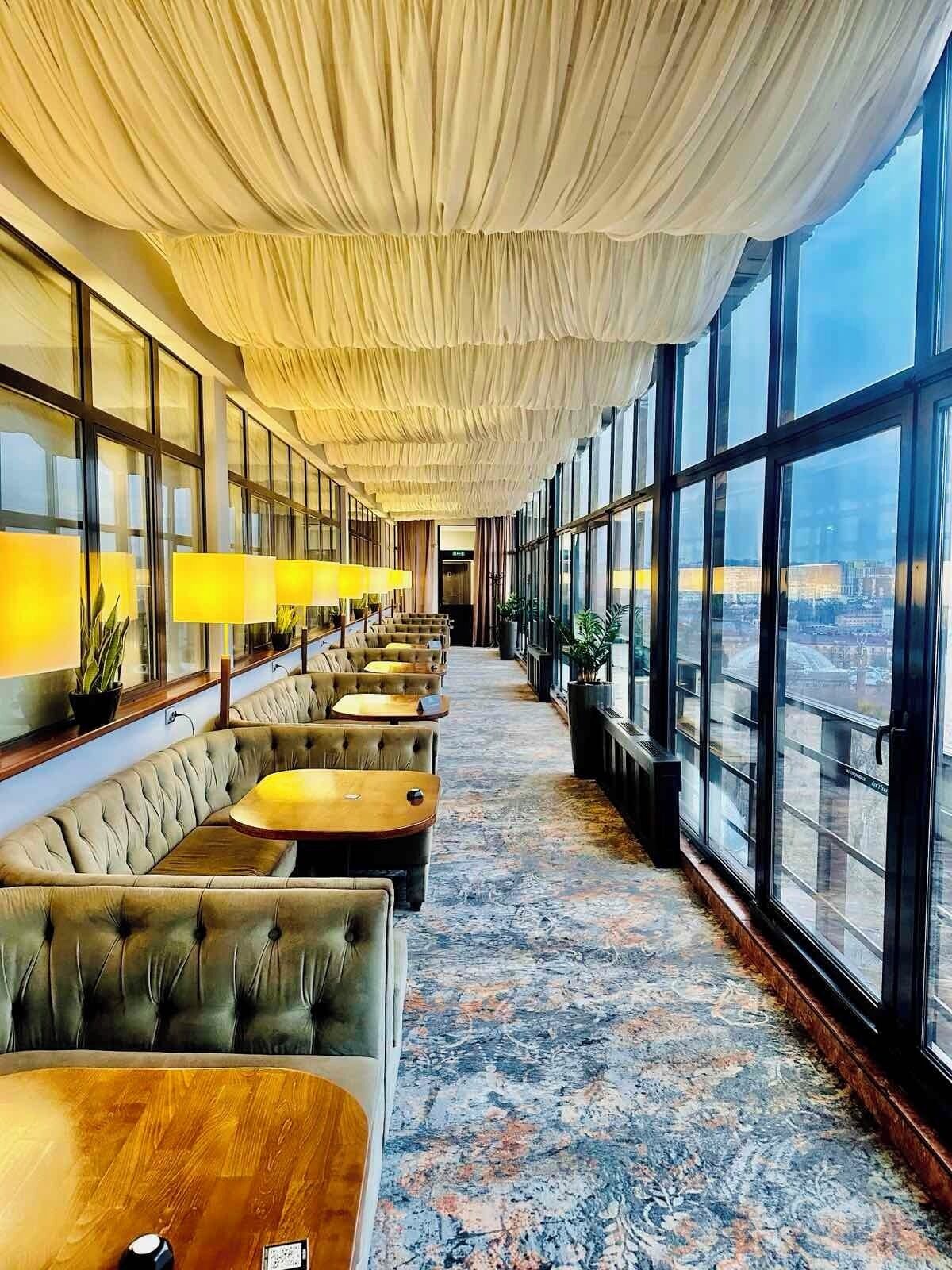A hotel lobby with a row of plush seating, large windows, and a patterned carpet.