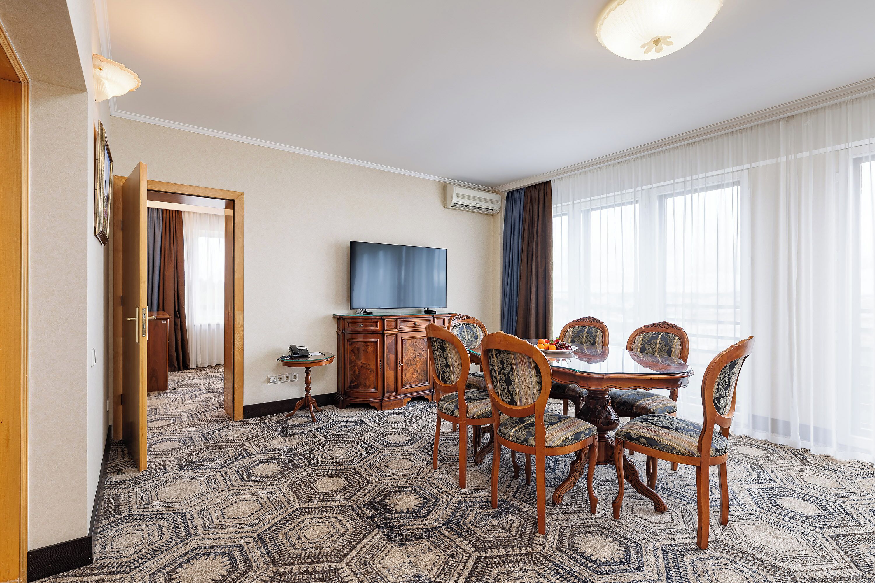 Ein Hotelzimmer mit Essbereich, ausgestattet mit einem runden Tisch, Stühlen, einem Fernseher und einem gemusterten Teppich.