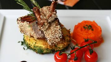 A white plate with a lamb chop, a carrot puree, and cherry tomatoes.