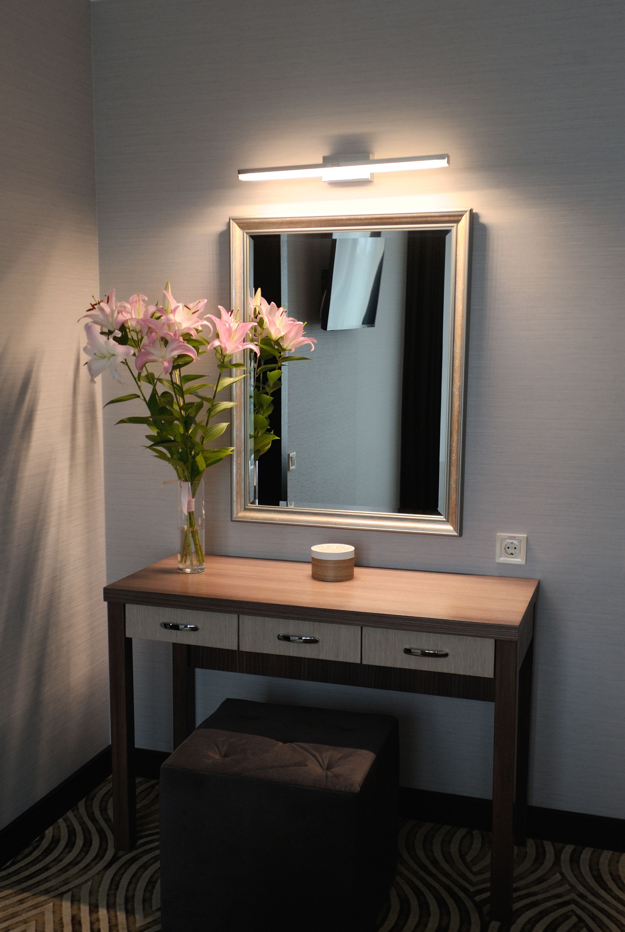 Une coiffeuse en bois avec un miroir, un vase de fleurs et une bougie.