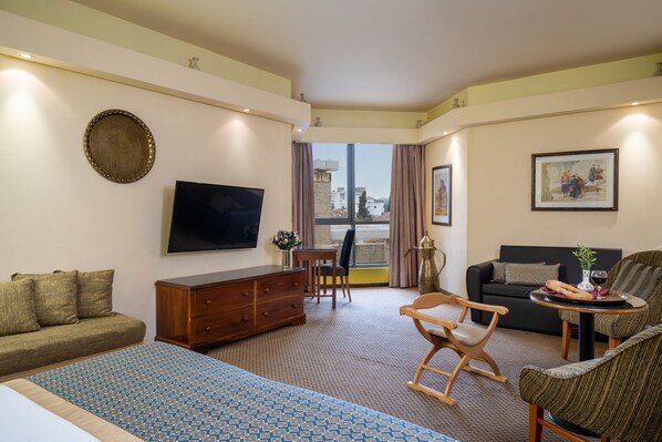 A hotel room with a bed, a sofa, a TV, a dining table, and a chair. - Olive Tree Hotel (Jerusalem)