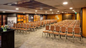 A conference room with rows of chairs, a carpeted floor, and a wall with bookshelves.