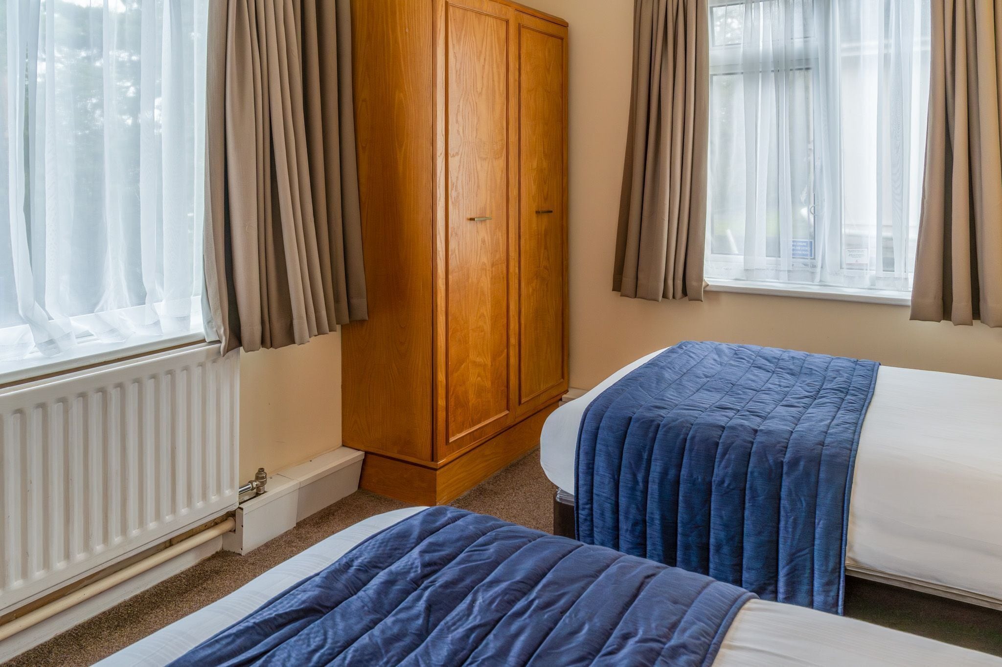 A bedroom with two beds, a wooden wardrobe, and a window with curtains.