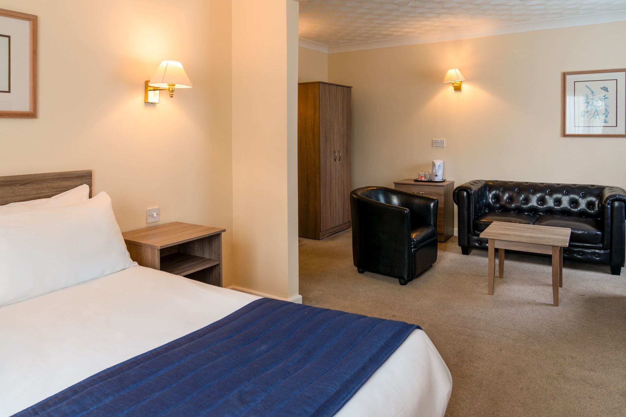 A hotel room with a bed, a small table, a leather sofa, a cabinet, and two wall-mounted lamps.