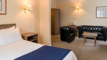 A hotel room with a bed, a small table, a leather sofa, a cabinet, and two wall-mounted lamps.