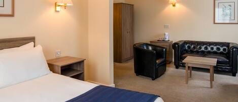 A hotel room with a bed, a small table, a leather sofa, a cabinet, and two wall-mounted lamps.