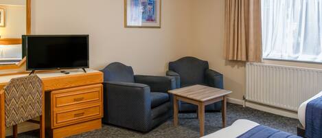 A hotel room with a bed, a desk with a TV, two armchairs, a small table, and a radiator.