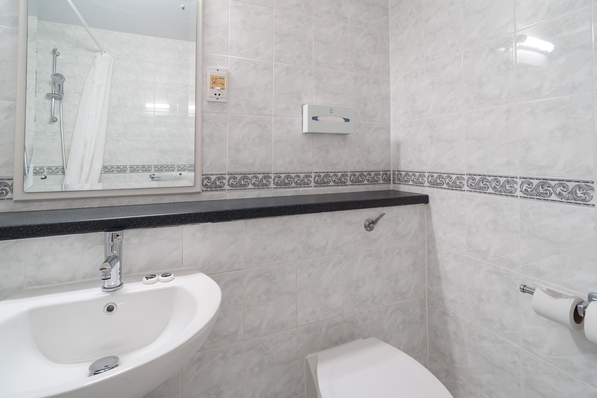 Ein Badezimmer mit Waschbecken, Spiegel, Dusche, Toilette und Handtuchspender.