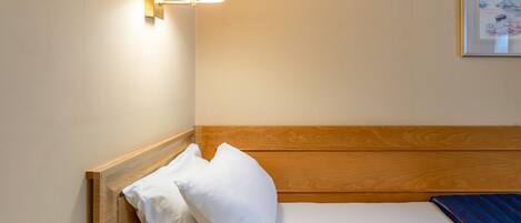 A hotel room with a wooden headboard, a single bed with white bedding, a wall-mounted lamp, and a framed picture on the wall.