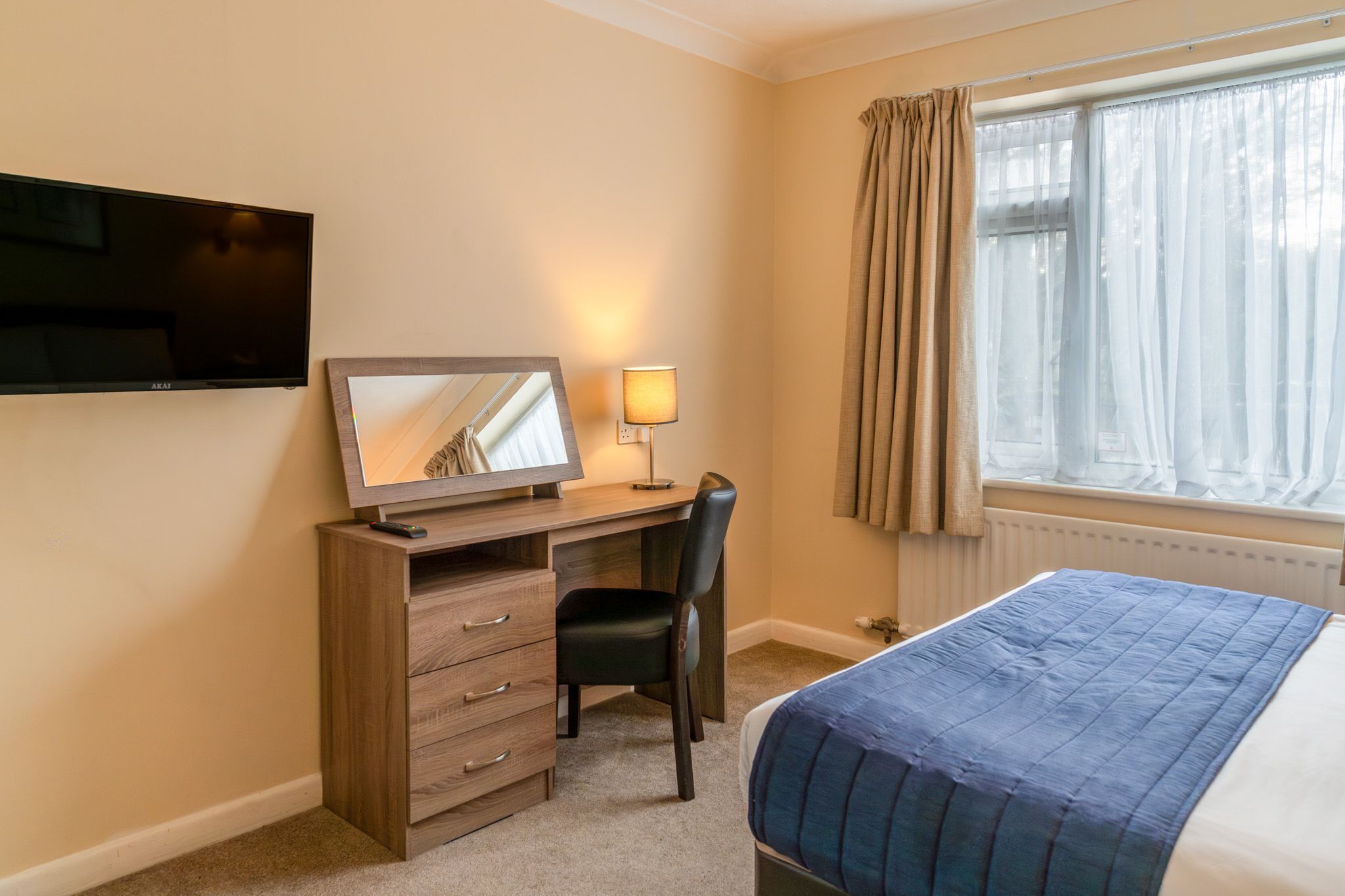 Une chambre d’hôtel comprenant un lit, un bureau avec une chaise, une télévision et une fenêtre avec des rideaux.