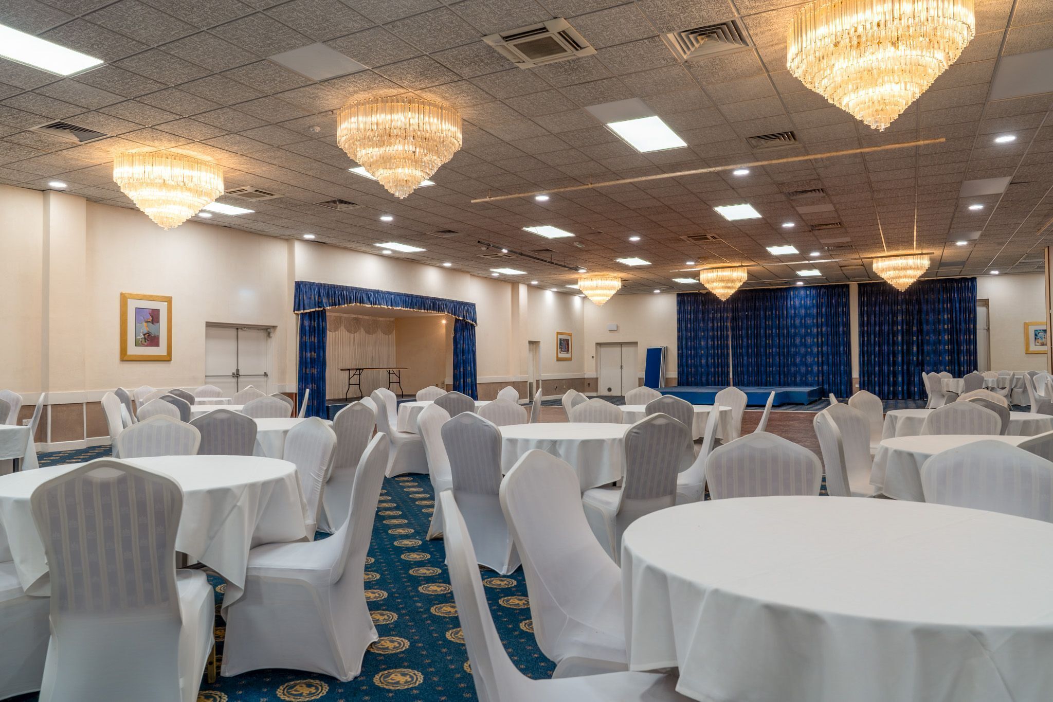 Un salón de banquetes con mesas redondas, sillas blancas y candelabros.