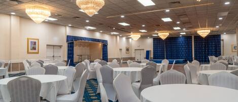 Un salón de banquetes con mesas redondas, sillas blancas y candelabros.