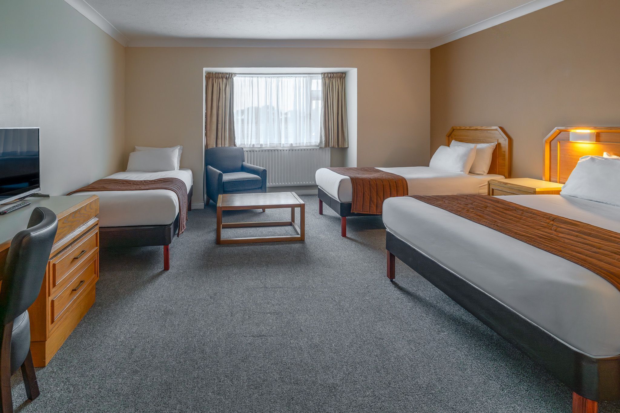 Habitación de hotel con dos camas, un escritorio con silla, televisor y ventana con cortinas.
