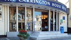 L'ingresso dell'Hotel Carrington House con una scala visibile che conduce alla porta, una pianta in vaso e un cestino blu.