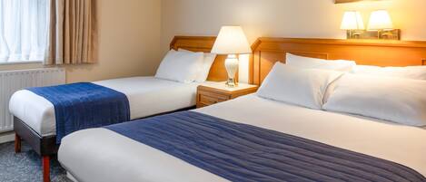A hotel room with two beds, a nightstand with a lamp, a window with curtains, and a painting on the wall.