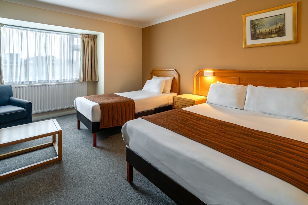 A hotel room with two beds, a desk, a chair, a radiator, and a window with curtains.