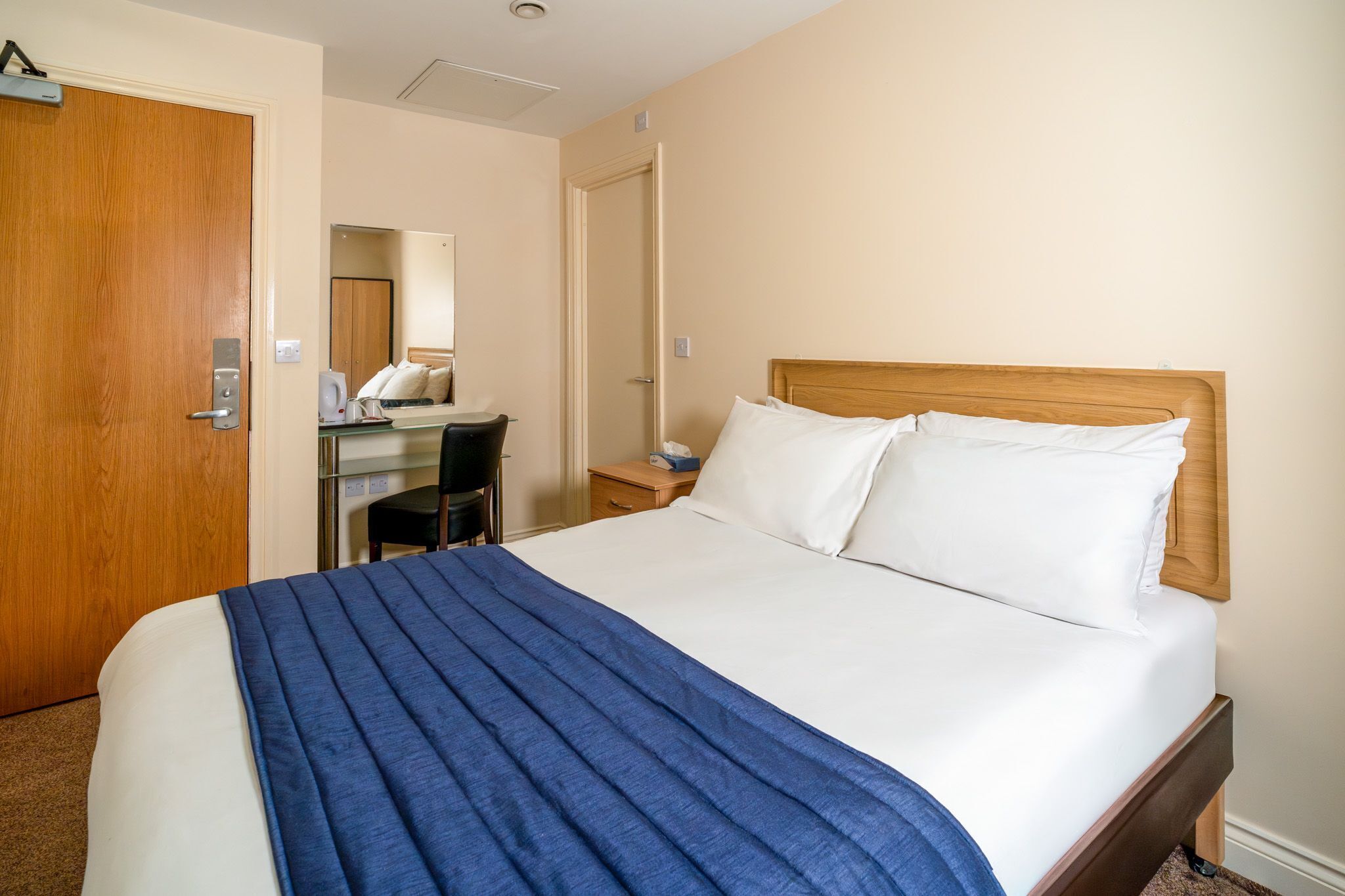 Una camera d'albergo con un letto, una scrivania con una sedia, uno specchio e una porta.
