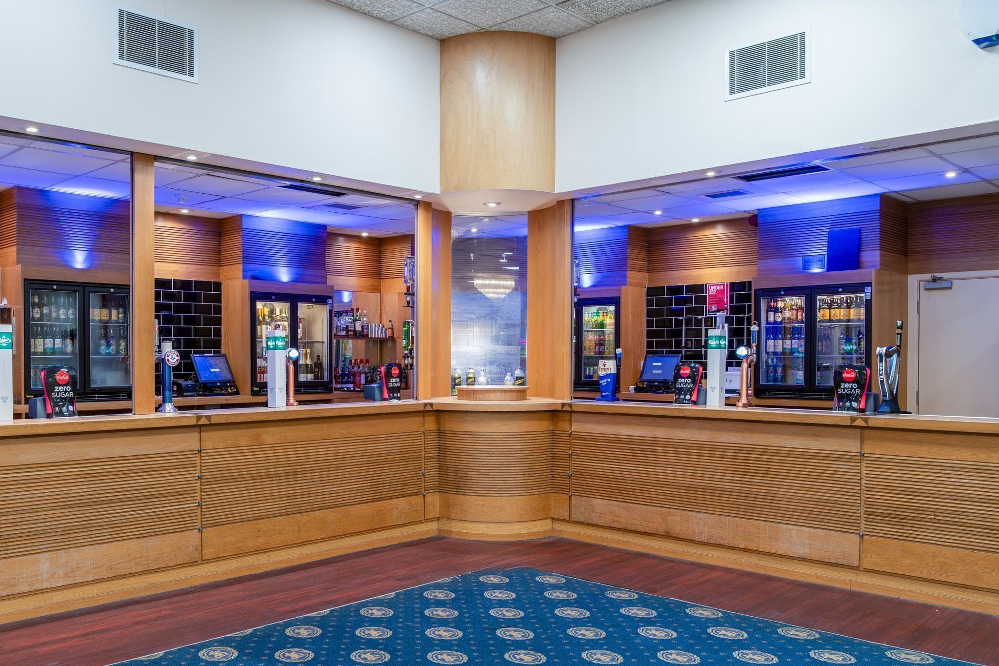 A lobby with a central pillar, wooden paneling, and a blue patterned carpet.