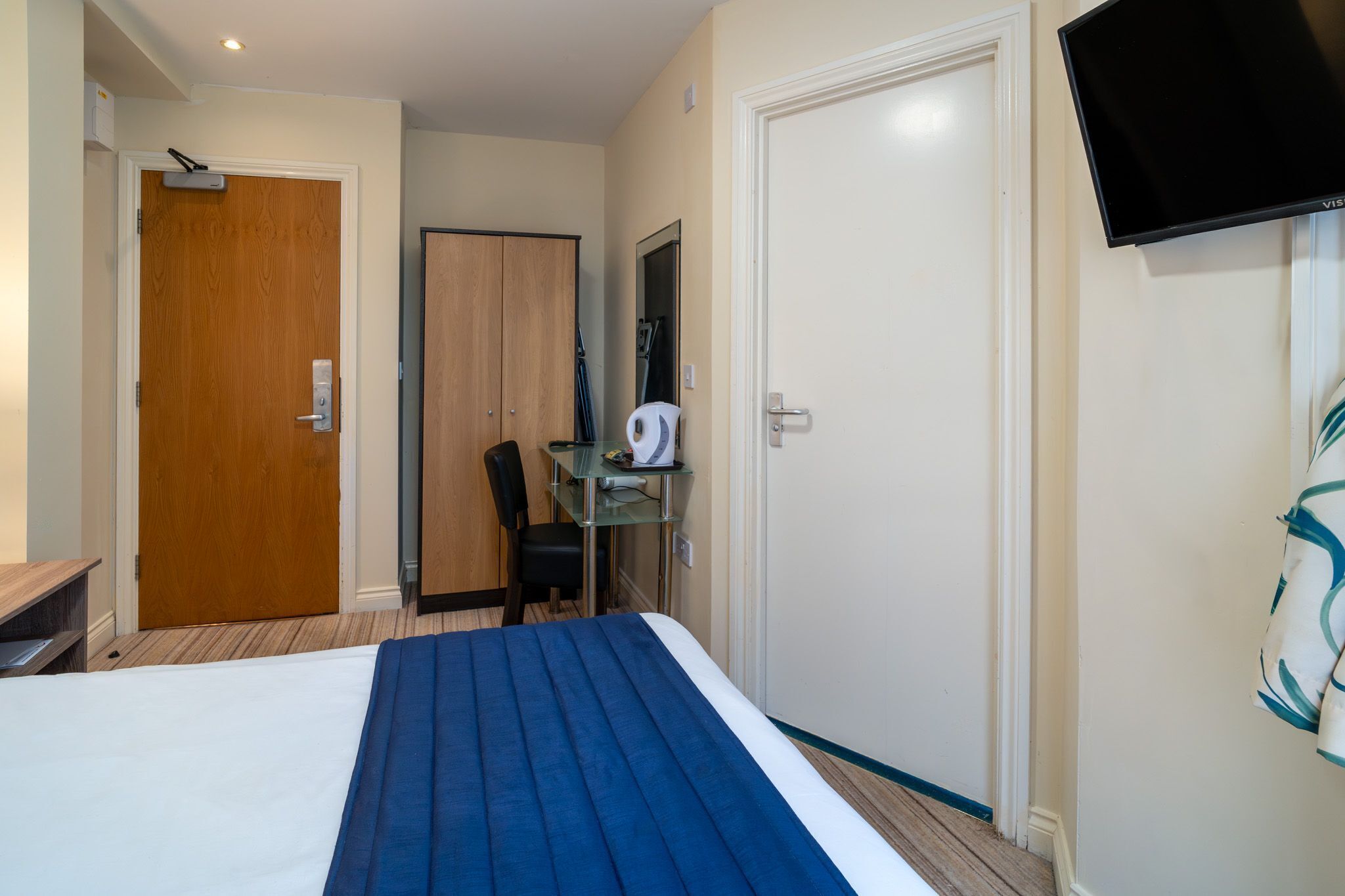 A hotel room with a bed, a desk, a chair, a television, and a door.