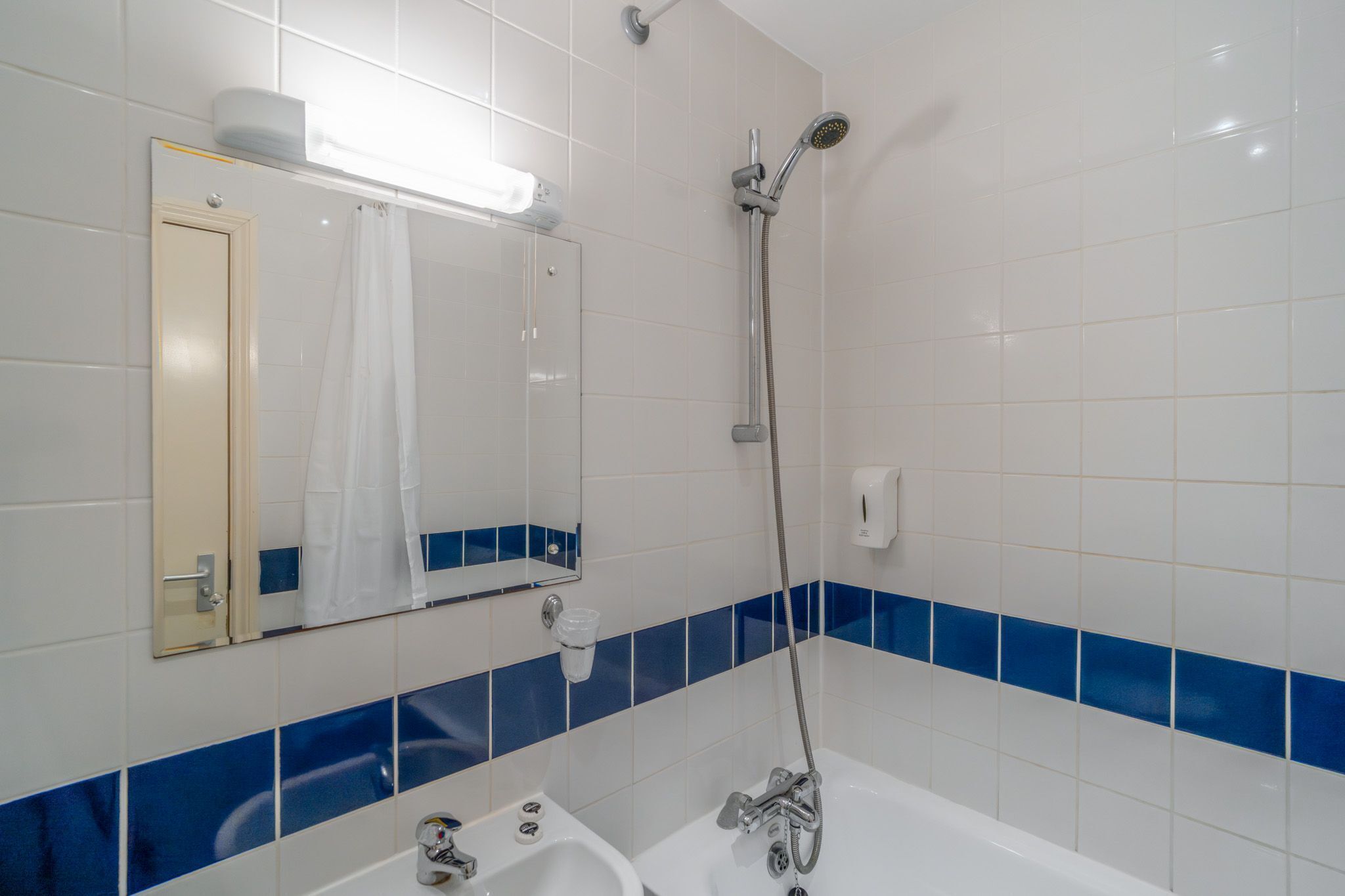 A bathroom with a bathtub, a shower, a sink, a mirror, and blue-tiled walls.