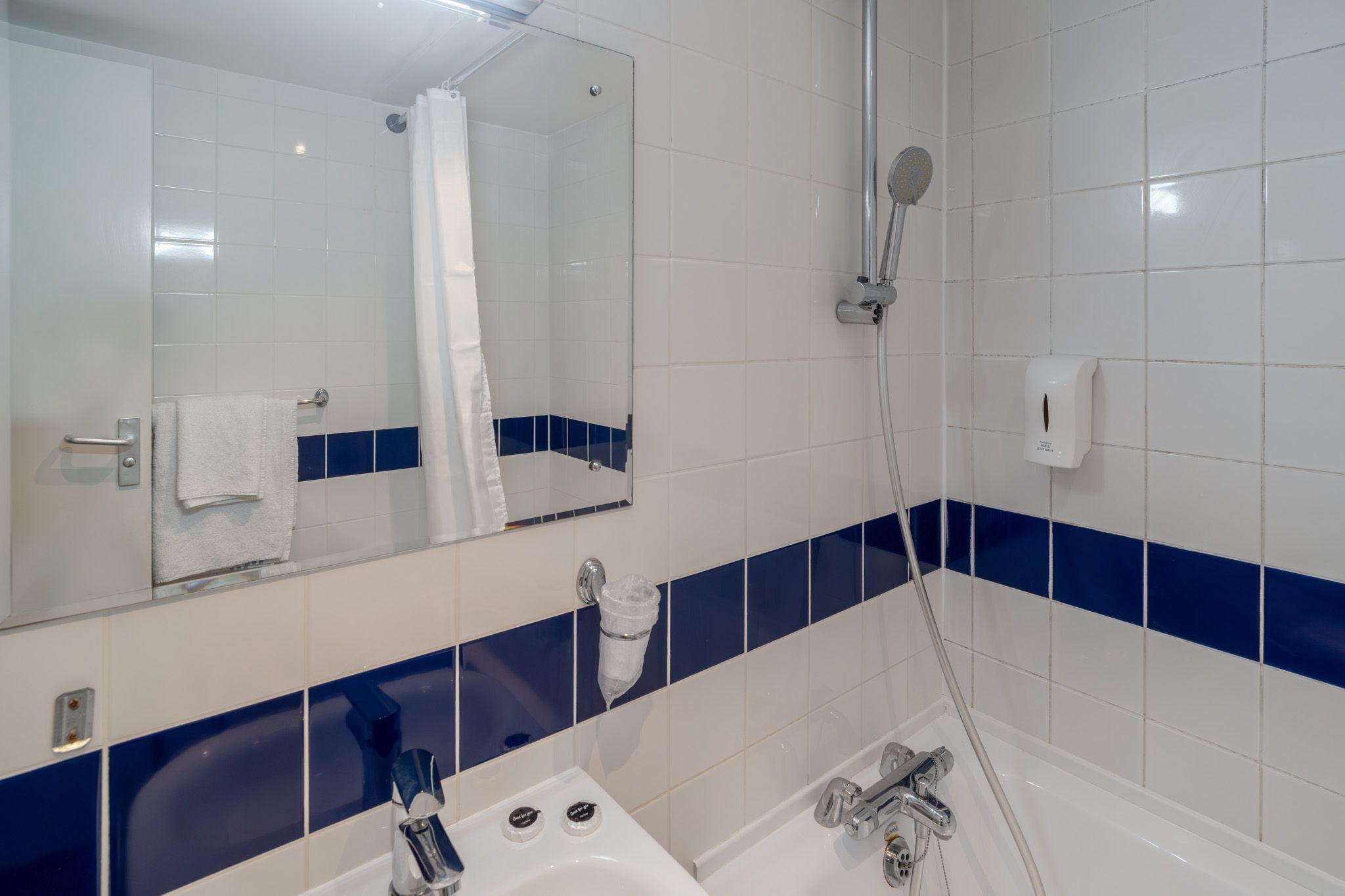 A bathroom with a white sink, a mirror, a shower, and blue-tiled walls.