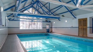 Una piscina interna con travi strutturali blu, pavimento piastrellato e una finestra con persiane.
