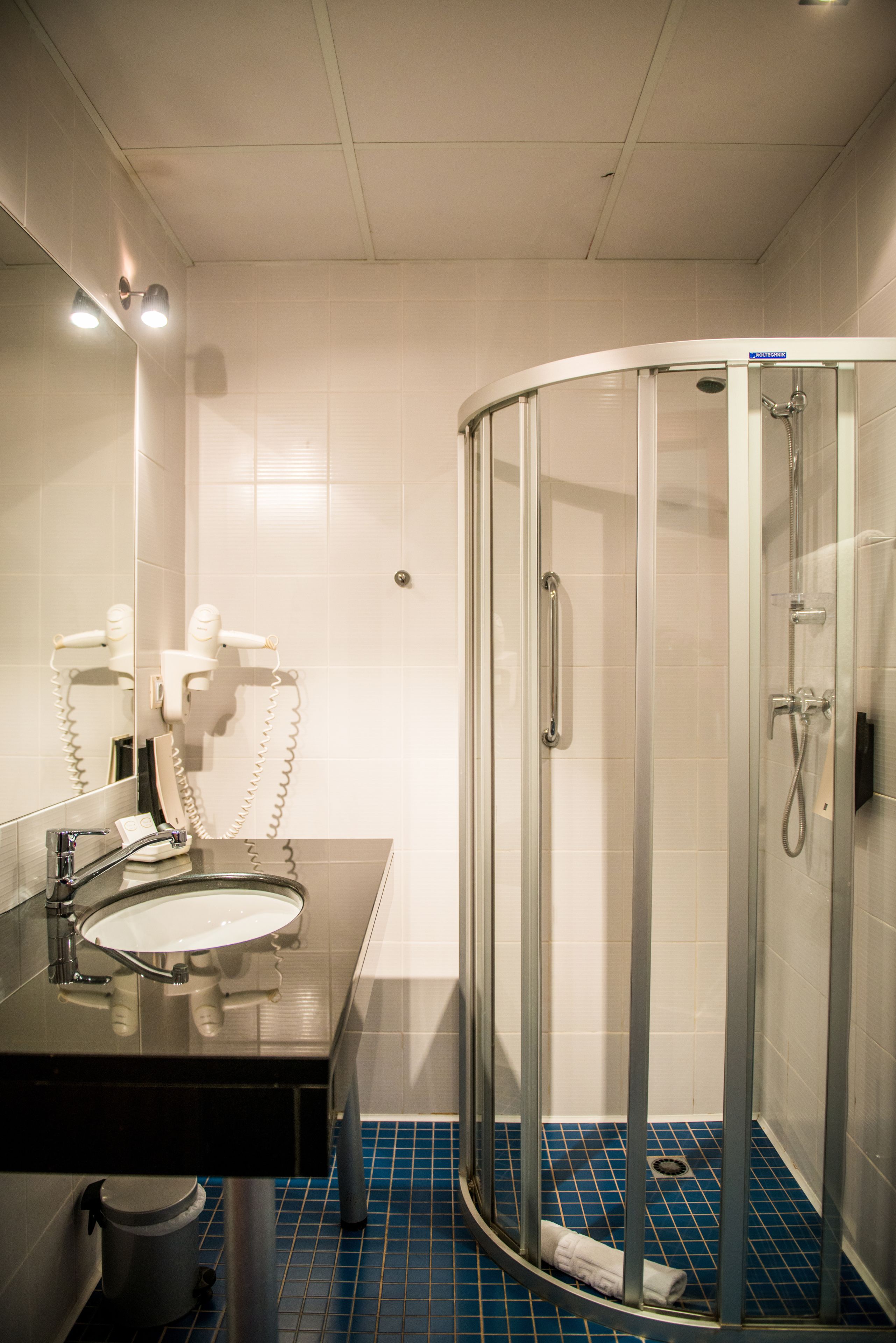 A bathroom with a sink, mirror, hairdryer, and a glass-enclosed shower.
