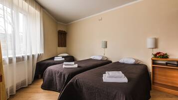 A hotel room with two beds, a wooden dresser, a nightstand, a lamp, and a window with sheer curtains.