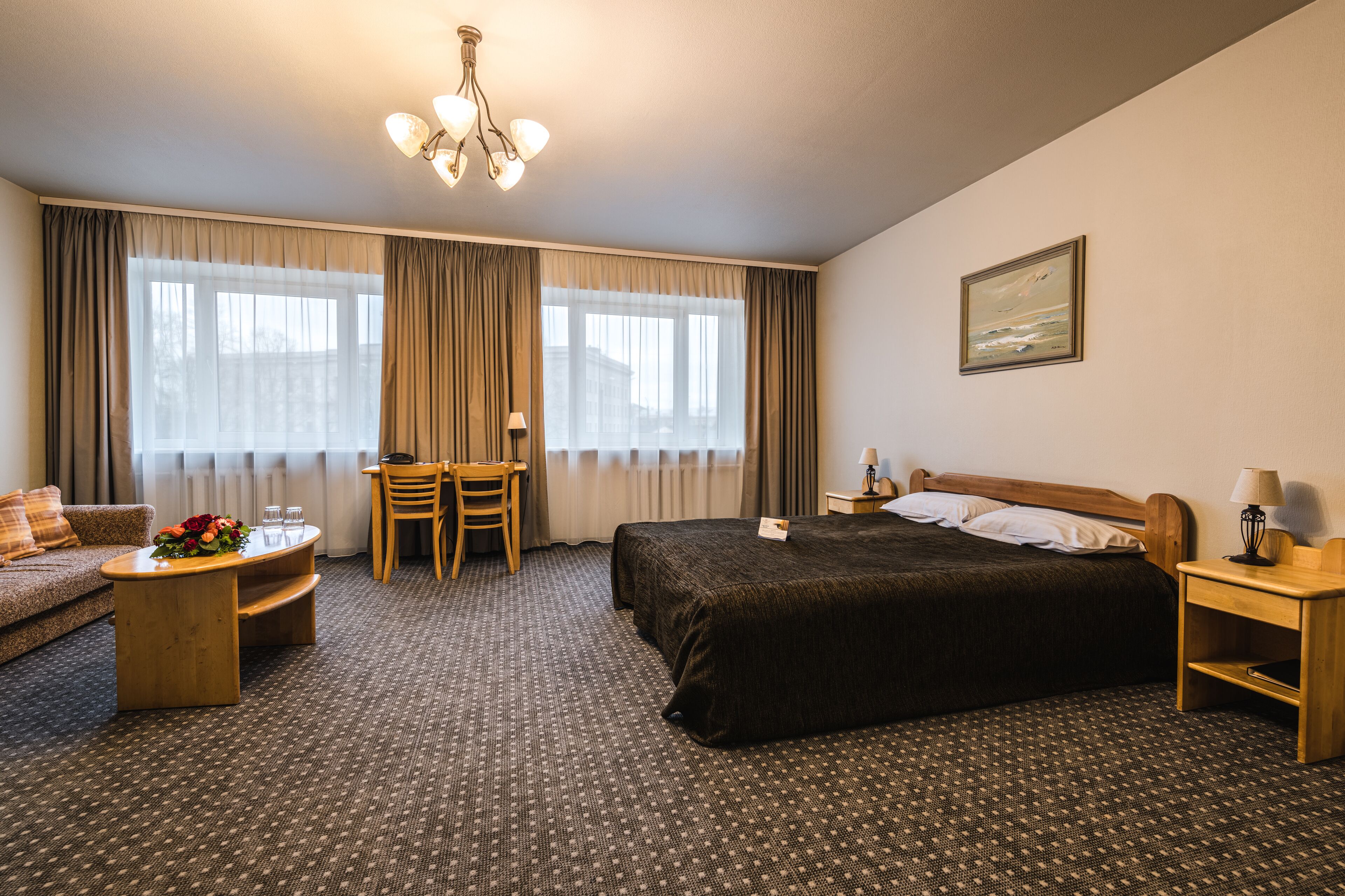 A hotel room with a large bed, a desk, a chair, a sofa, and a chandelier.