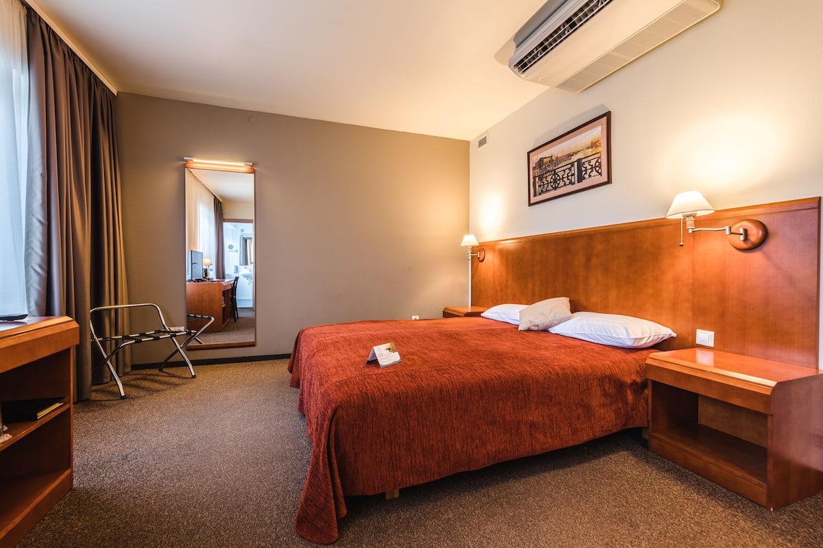 Quarto de hotel com uma cama grande, uma escrivaninha, uma cadeira e um espelho.