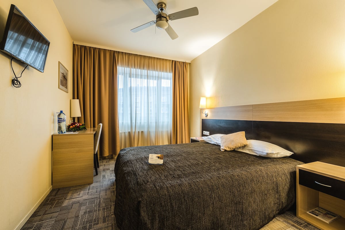 Quarto de hotel com uma cama, uma escrivaninha com abajur, televisão e ventoinha no teto.