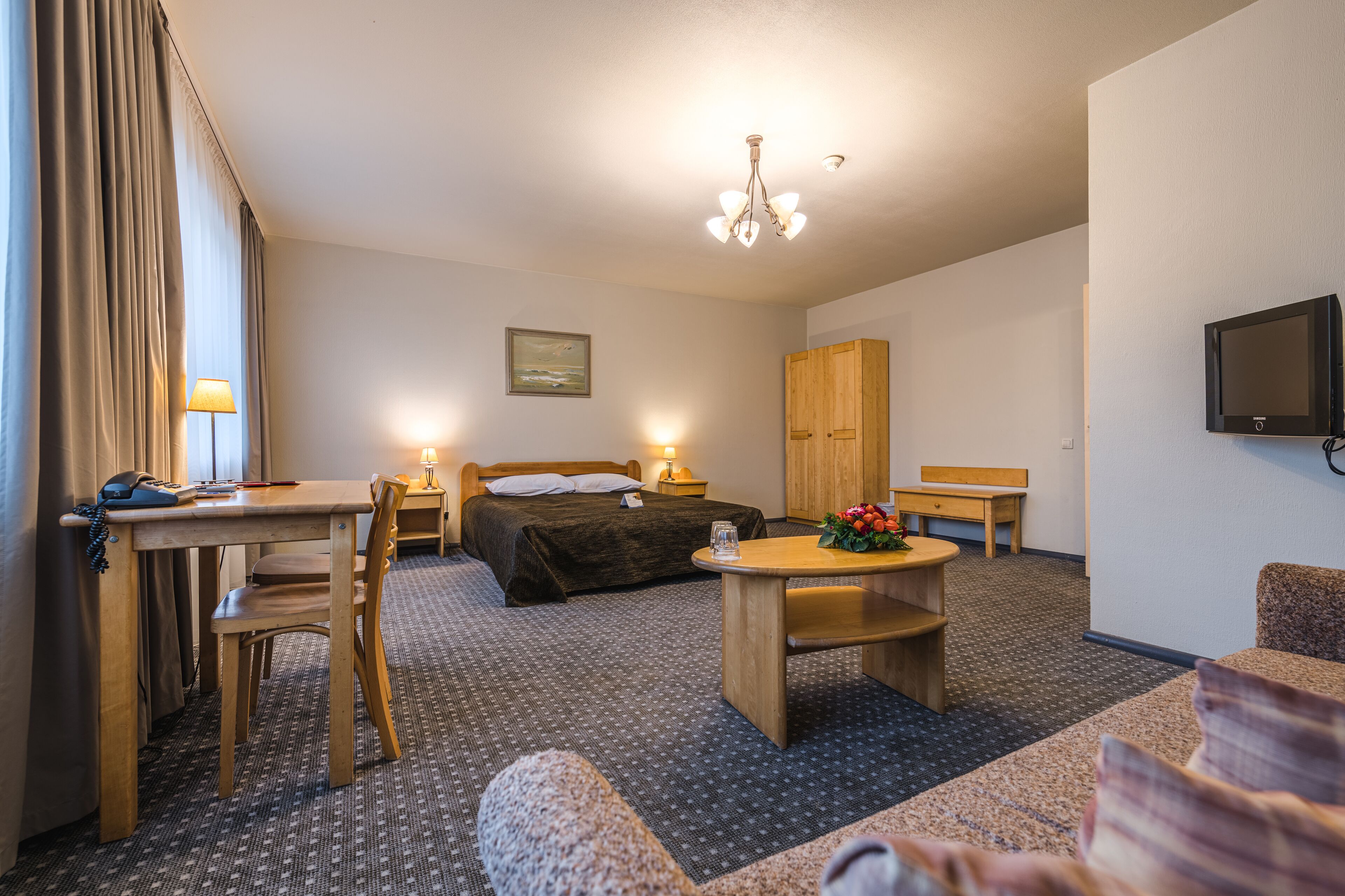 Habitación de hotel con cama, escritorio, silla, mesa, televisor y un cuadro en la pared.