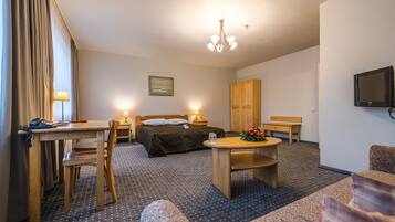 Habitación de hotel con cama, escritorio, silla, mesa, televisor y un cuadro en la pared.