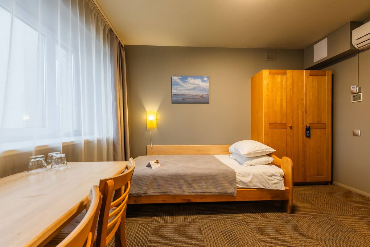 Quarto de hotel com cama de madeira, mesa de jantar com cadeiras, luminária na parede e um quadro.