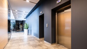 A modern hallway with a marble floor, a potted plant, and an elevator. - Liva Hotel (Liepaja)
