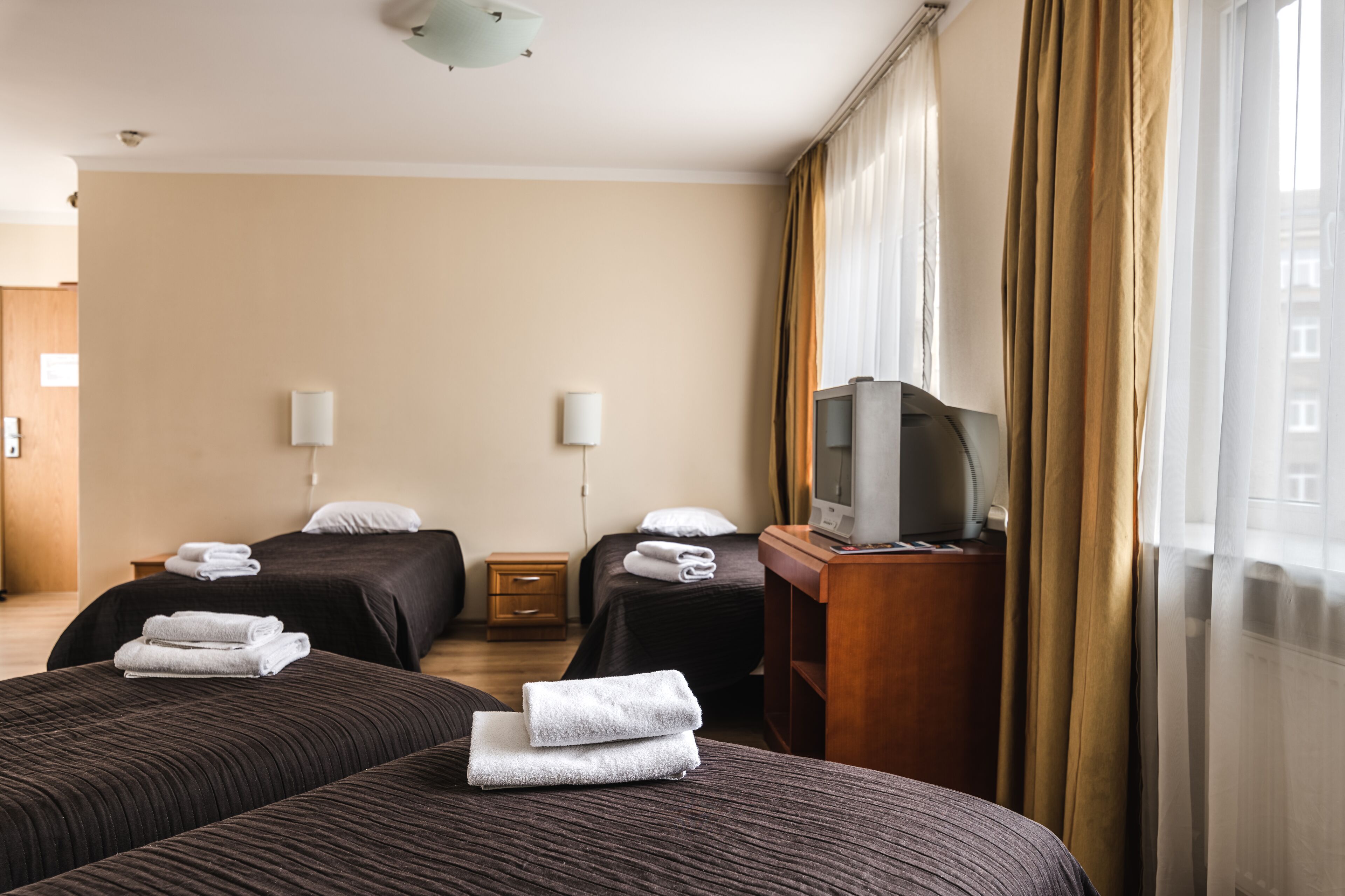 A hotel room with two beds, a TV on a wooden stand, and a window with curtains.