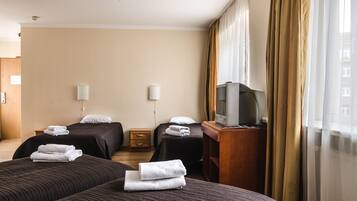A hotel room with two beds, a TV on a wooden stand, and a window with curtains.
