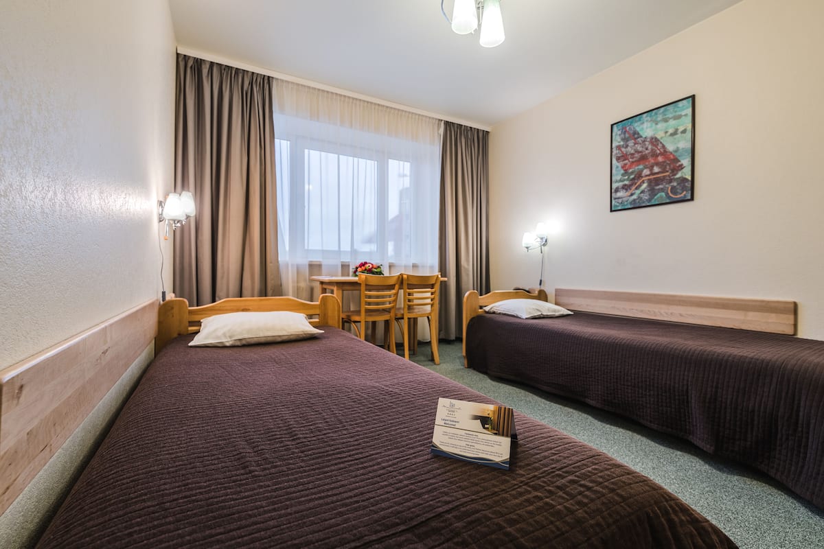Quarto de hotel com duas camas, uma escrivaninha, uma cadeira e um quadro na parede.