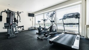 A gym with various exercise equipment, large windows, and a flat-screen TV. - Liva Hotel (Liepaja)