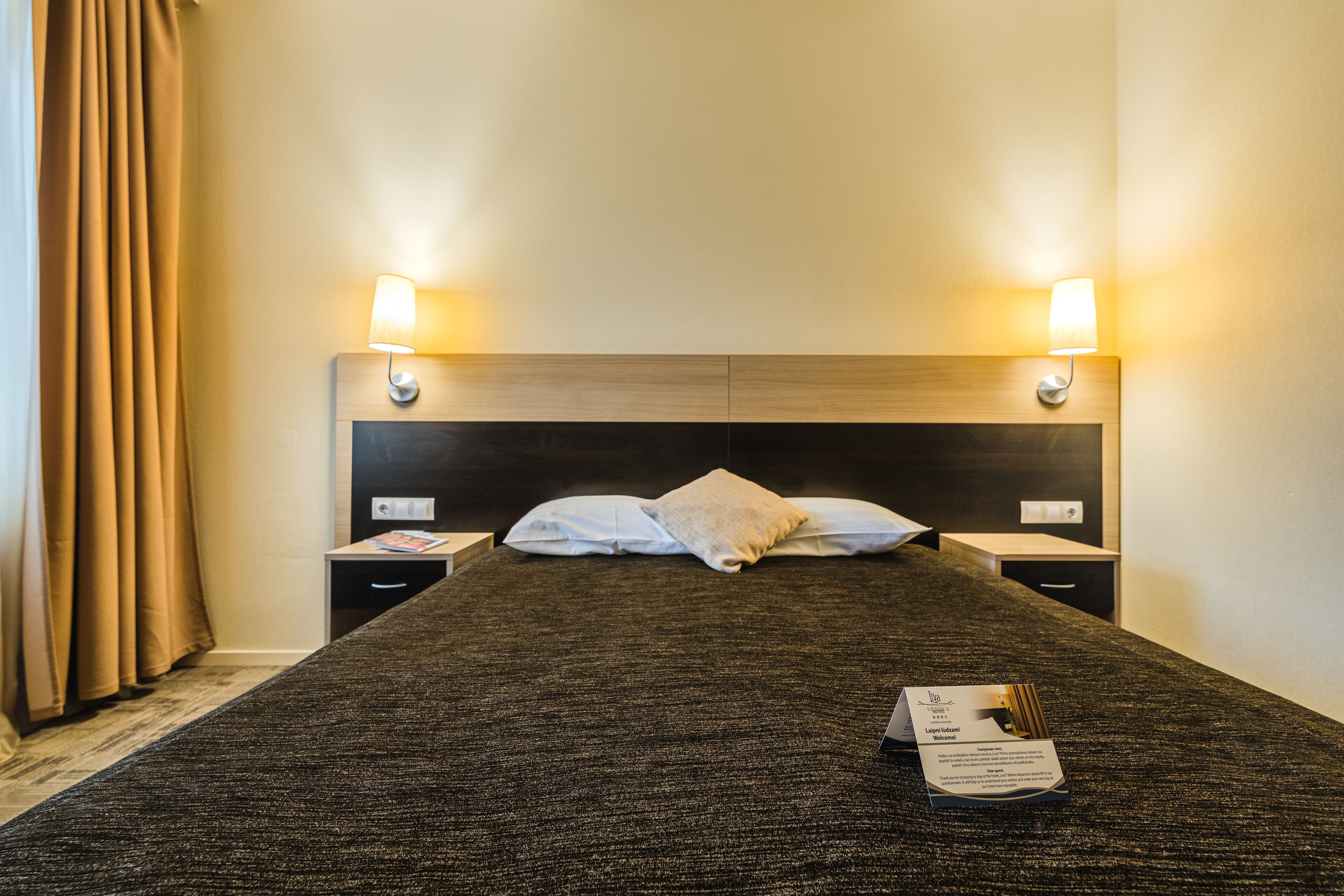 Una cama bien hecha con un cabecero oscuro, dos lámparas de noche y un par de almohadas.