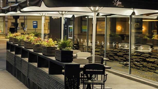 An outdoor seating area with tables and chairs under a large umbrella, in front of a building with the sign "RESTAURANTS". - Liva Hotel (Liepaja)