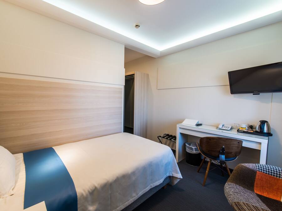 Una habitación de hotel con cama, escritorio, silla, televisor y basurero.