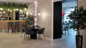 A modern interior with a bar area, a round table with chairs, and a large potted plant. - Amrita Hotel (Liepaja)