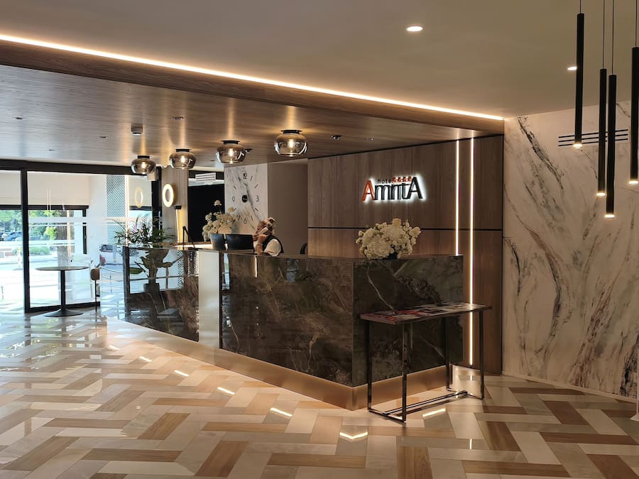 Uma área de recepção de hotel com um balcão de mármore, um relógio e uma luminária moderna.