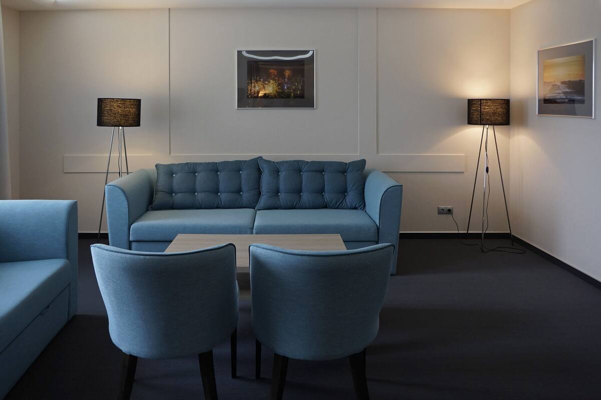 Una sala de estar moderna con un sofá azul, dos sillones, una mesa de centro y dos lámparas de pie.