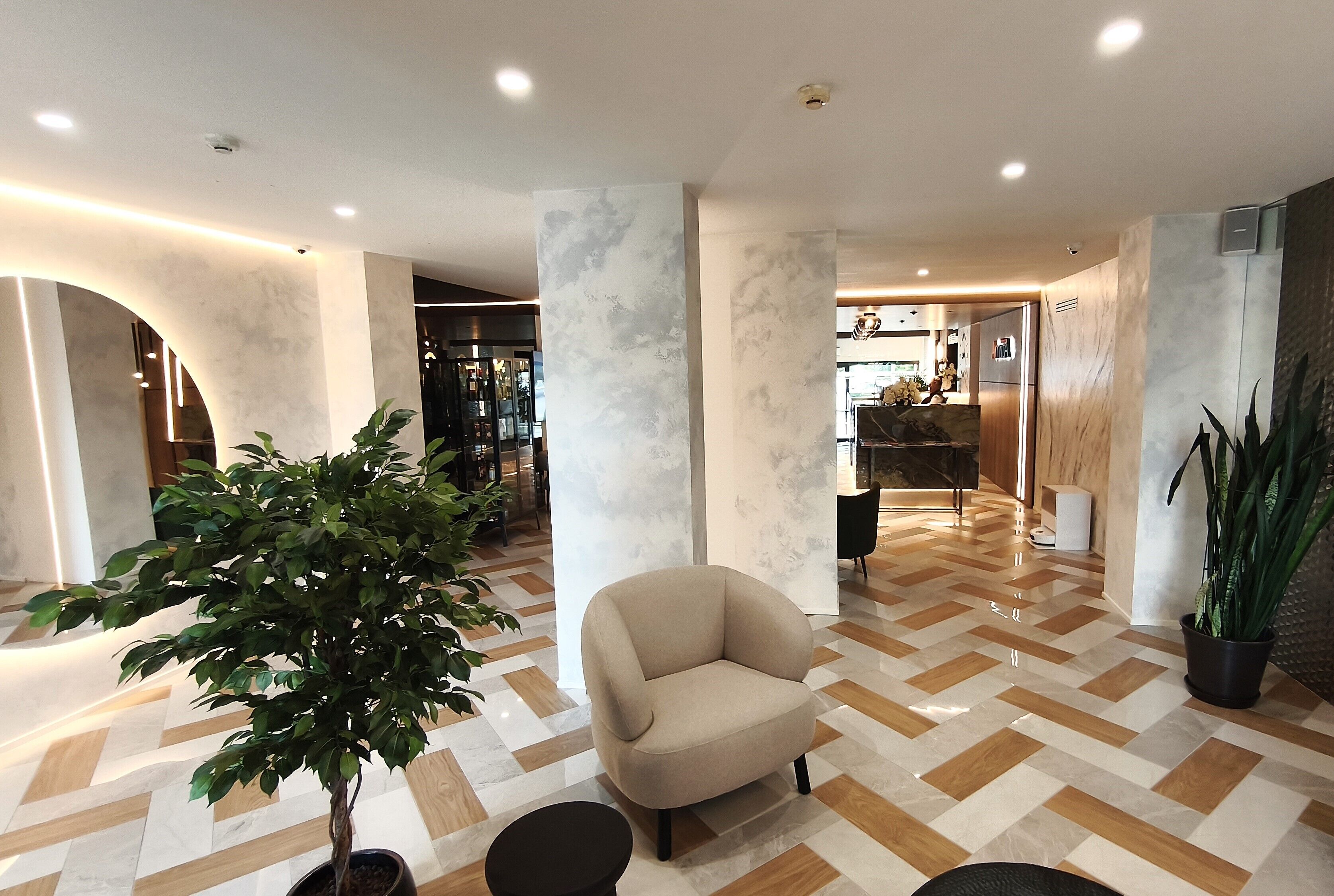 Un interior moderno con un sillón color beige, una planta en maceta y un suelo con patrón de espiga.